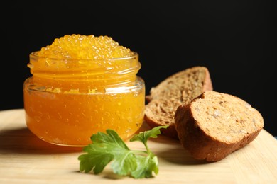 Fresh pike caviar in glass jar, bread and parsley on wooden board, closeup