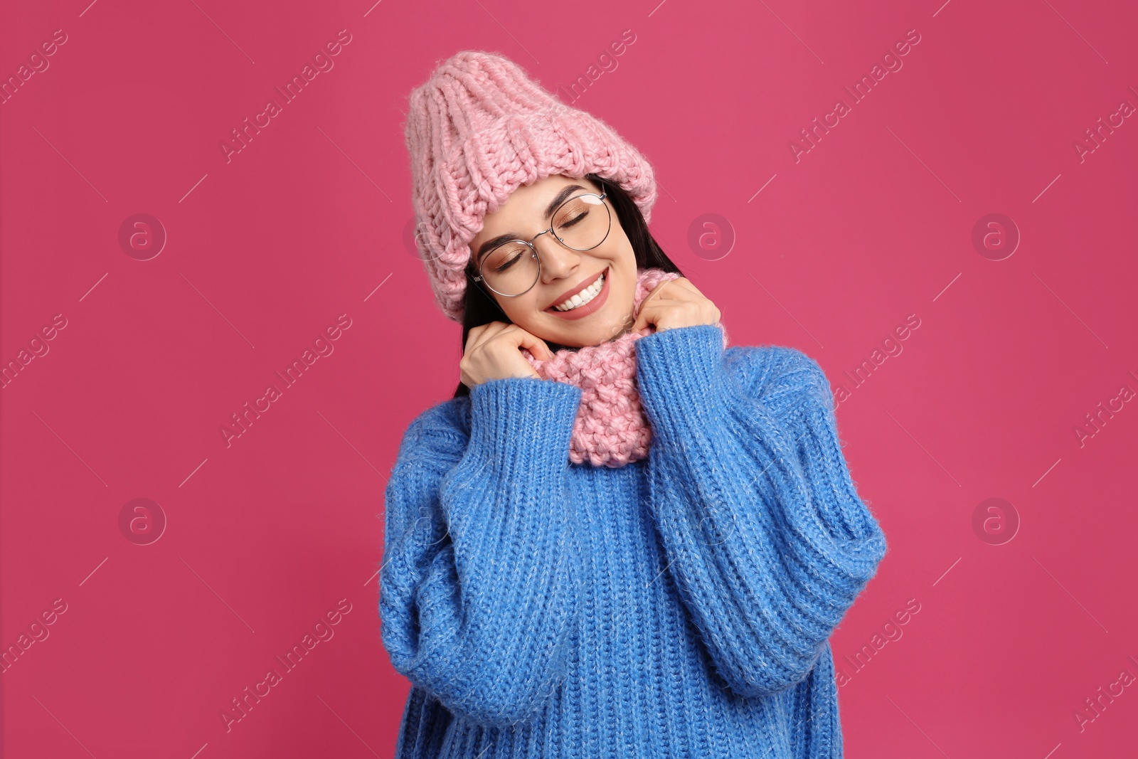 Photo of Young woman wearing warm sweater, snood and hat on crimson background. Winter season