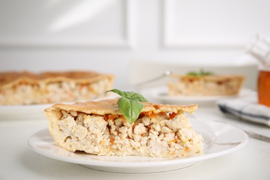 Piece of delicious pie with meat and basil on white table