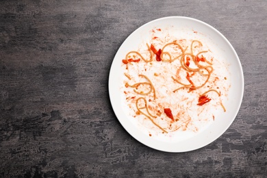 Dirty plate with food leftovers on grey background, top view. Space for text