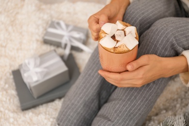 Young woman with cocoa sitting on light blanket, closeup. Christmas holiday