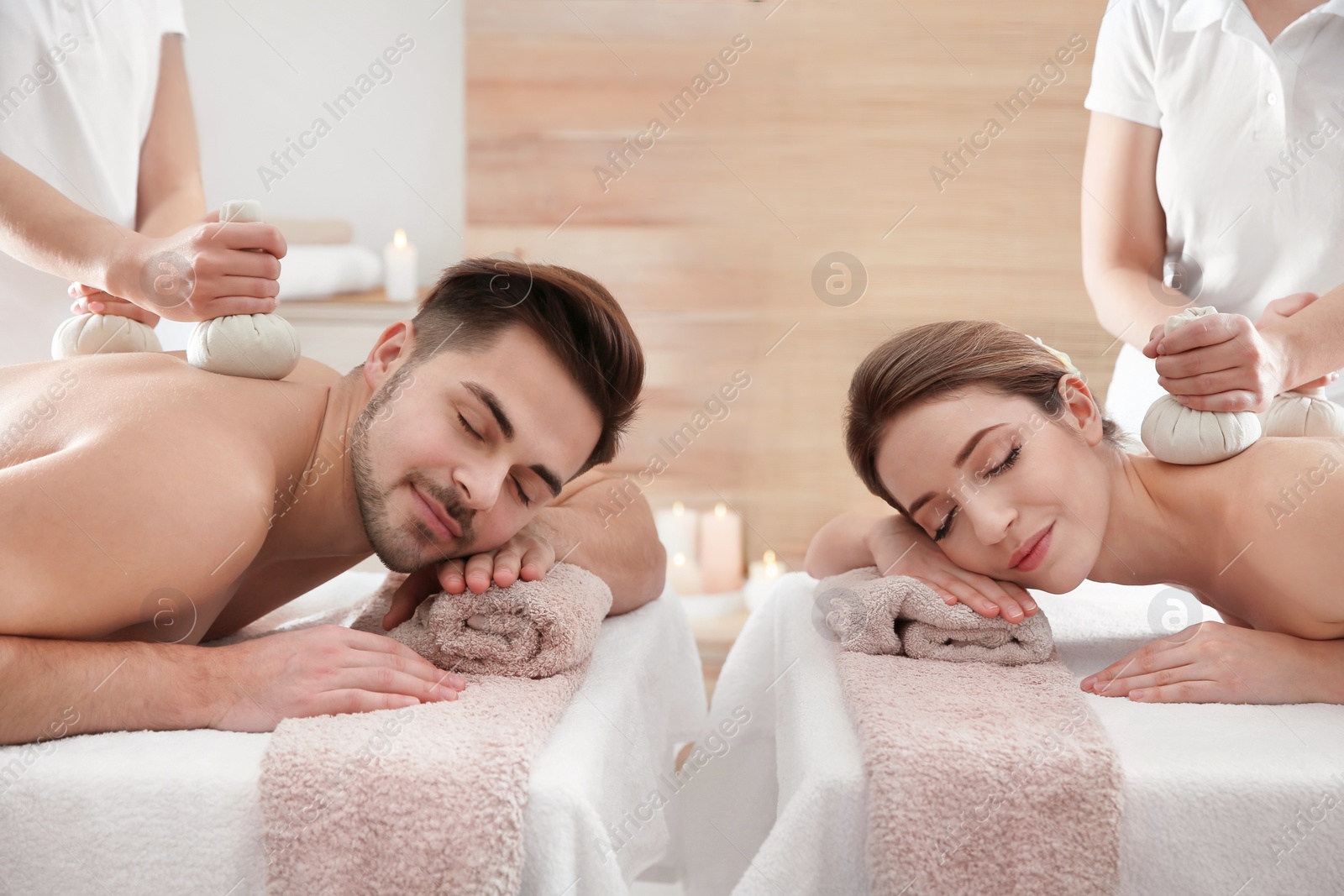 Photo of Romantic young couple enjoying herbal bag massage in spa salon