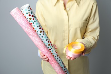 Photo of Woman holding different colorful wrapping paper rolls and ribbons on grey background, closeup
