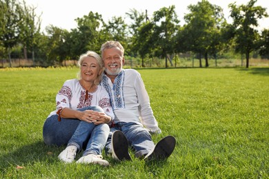 Photo of Happy mature couple in Ukrainian national clothes resting on green grass outdoors