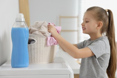 Photo of Little girl taking out dirty clothes from basket in bathroom