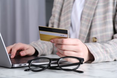 Photo of Online payment. Woman with laptop and credit card at white marble table, closeup