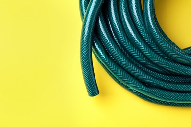 Photo of Green rubber watering hose on yellow background, top view. Space for text