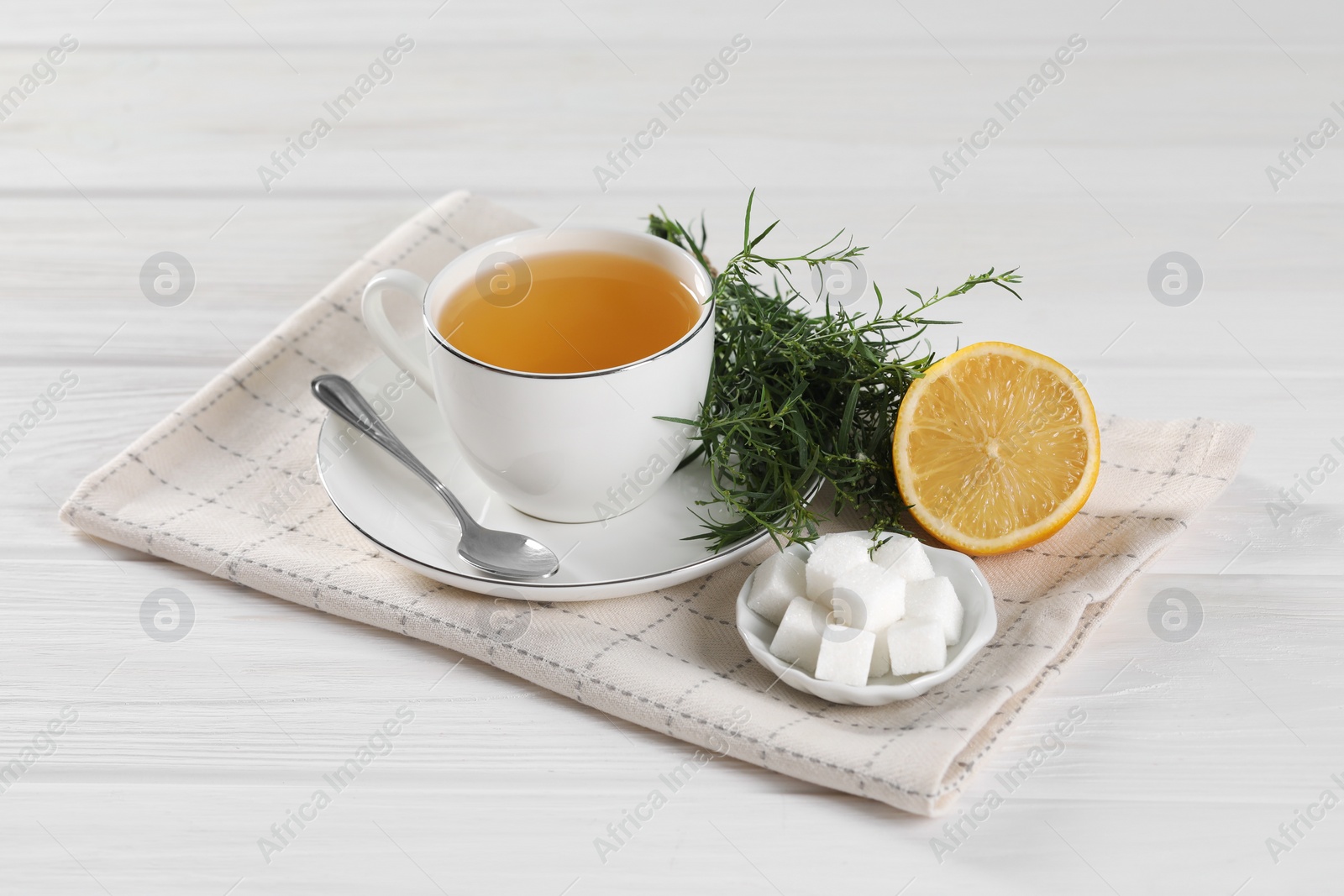 Photo of Aromatic herbal tea, fresh tarragon sprigs, sugar cubes and lemon on white wooden table