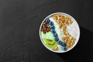Photo of Tasty smoothie bowl with fresh kiwi fruit, blueberries and oatmeal on black table, top view. Space for text