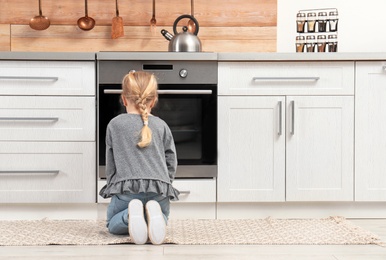 Little girl sitting near oven in kitchen. Space for text