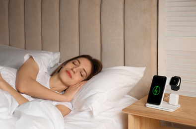 Photo of Smartphone, watch, earphones charging on wireless pad and sleeping woman in room