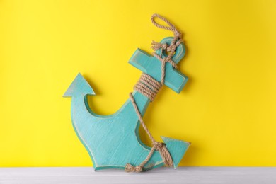 Anchor with hemp rope on white wooden table near yellow wall
