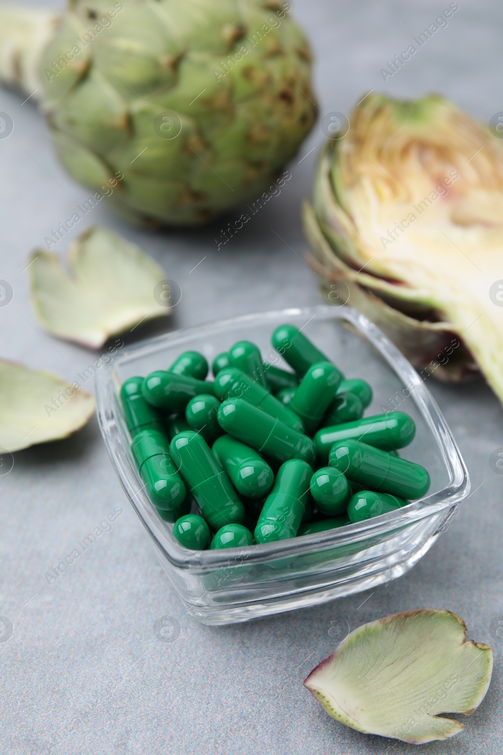 Photo of Bowl with pills and fresh artichokes on grey table, closeup