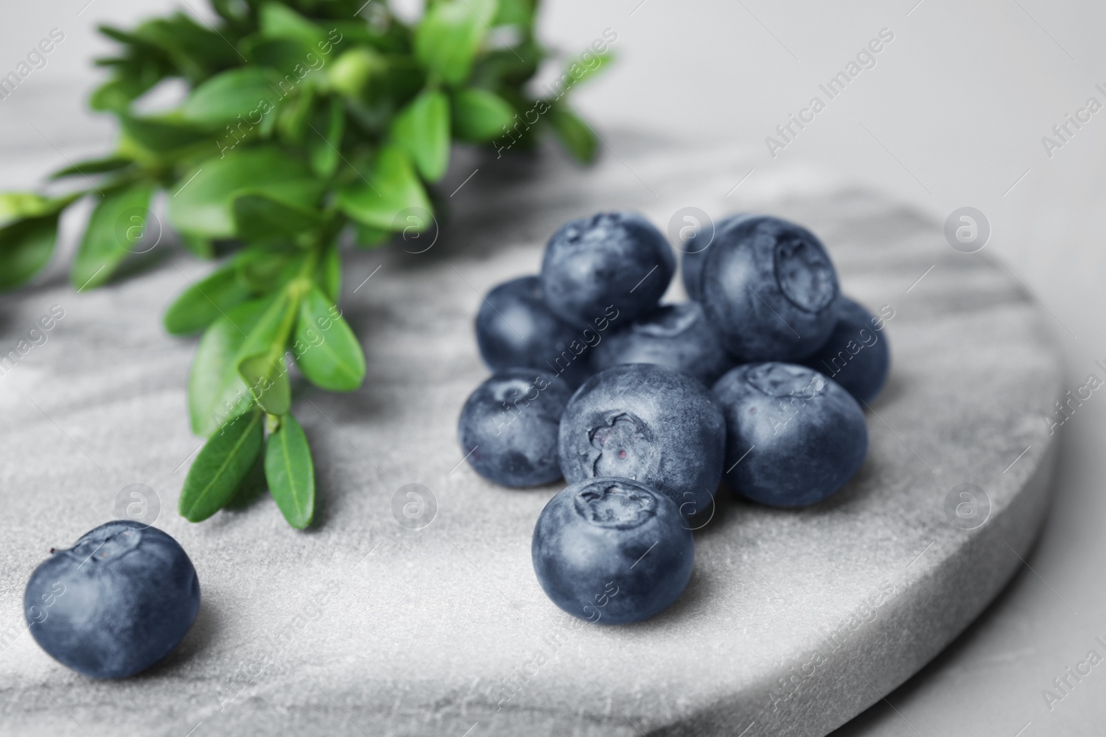 Photo of Marble board with tasty blueberries and leaves on grey table