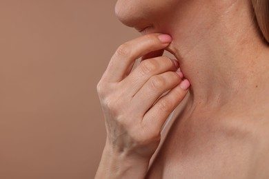 Mature woman touching her neck on beige background, closeup. Space for text