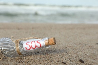 Glass bottle with SOS message on sand near sea, space for text