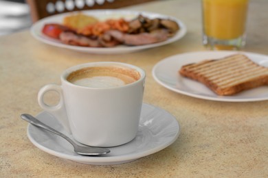 Cup of coffee and delicious breakfast served on beige table in cafe