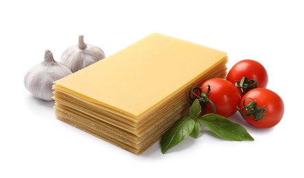 Photo of Stack of uncooked lasagna sheets, tomatoes and garlic isolated on white