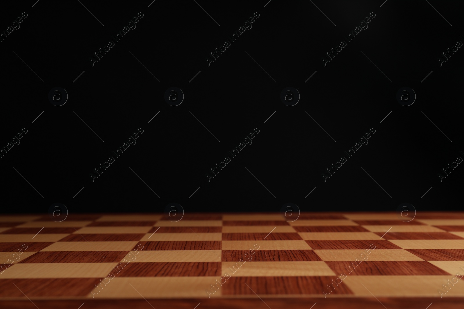 Photo of Empty wooden chess board against black background, closeup. Space for text