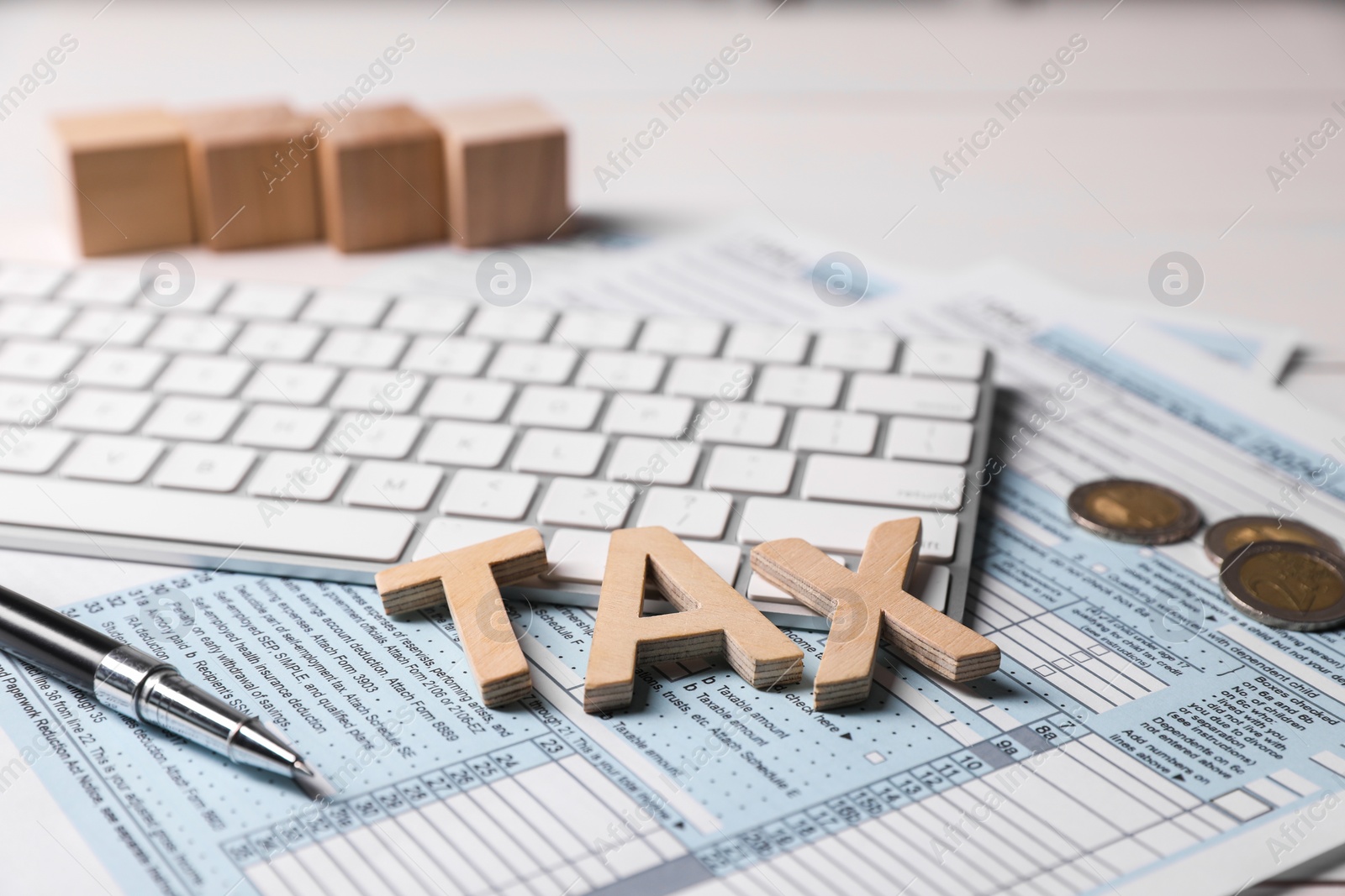 Photo of Word Tax made with wooden letters, documents, keyboard, coins and pen on white table, closeup
