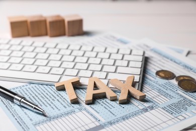 Word Tax made with wooden letters, documents, keyboard, coins and pen on white table, closeup