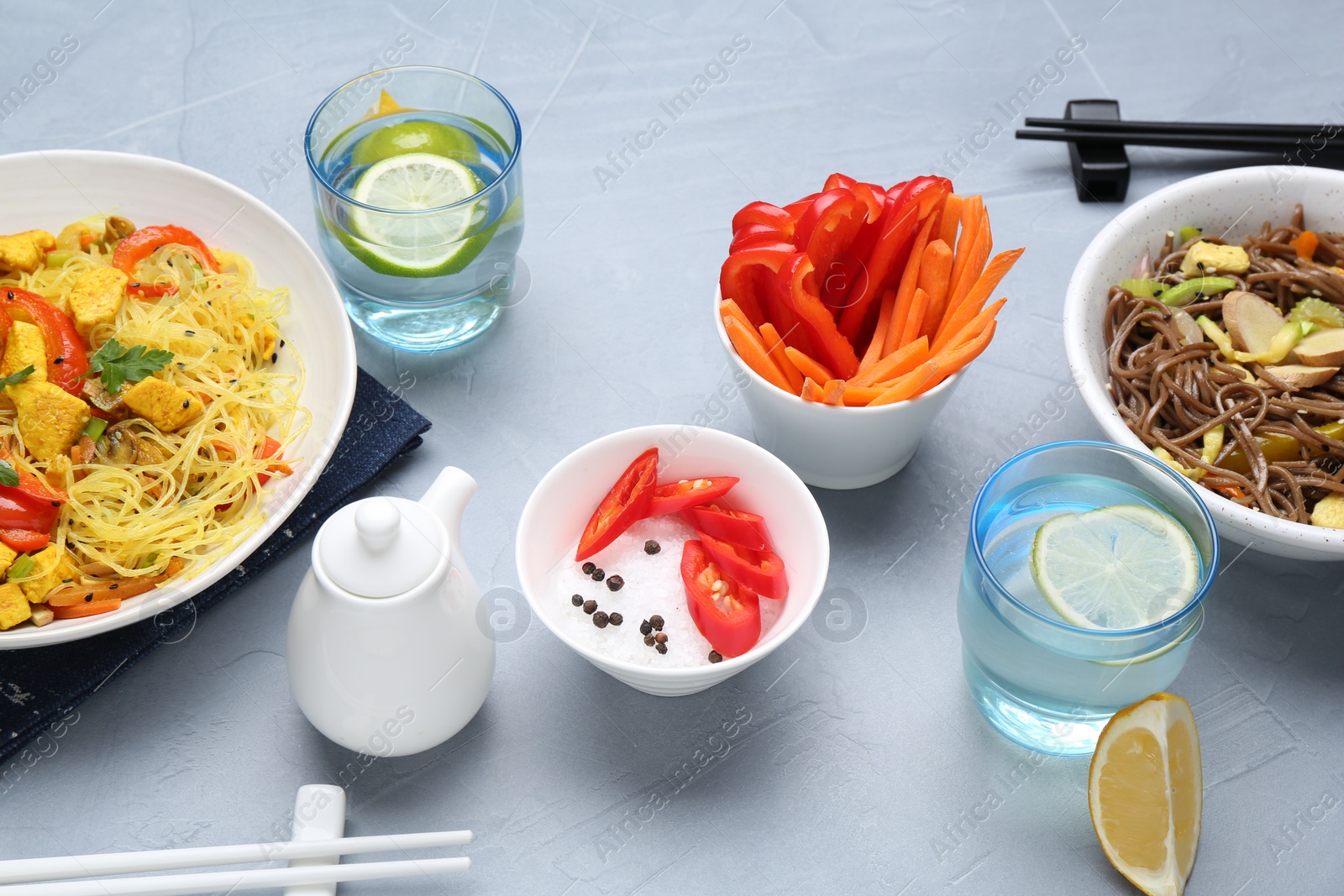 Photo of Stir-fry. Delicious cooked noodles with chicken and vegetables in bowls served on gray textured table