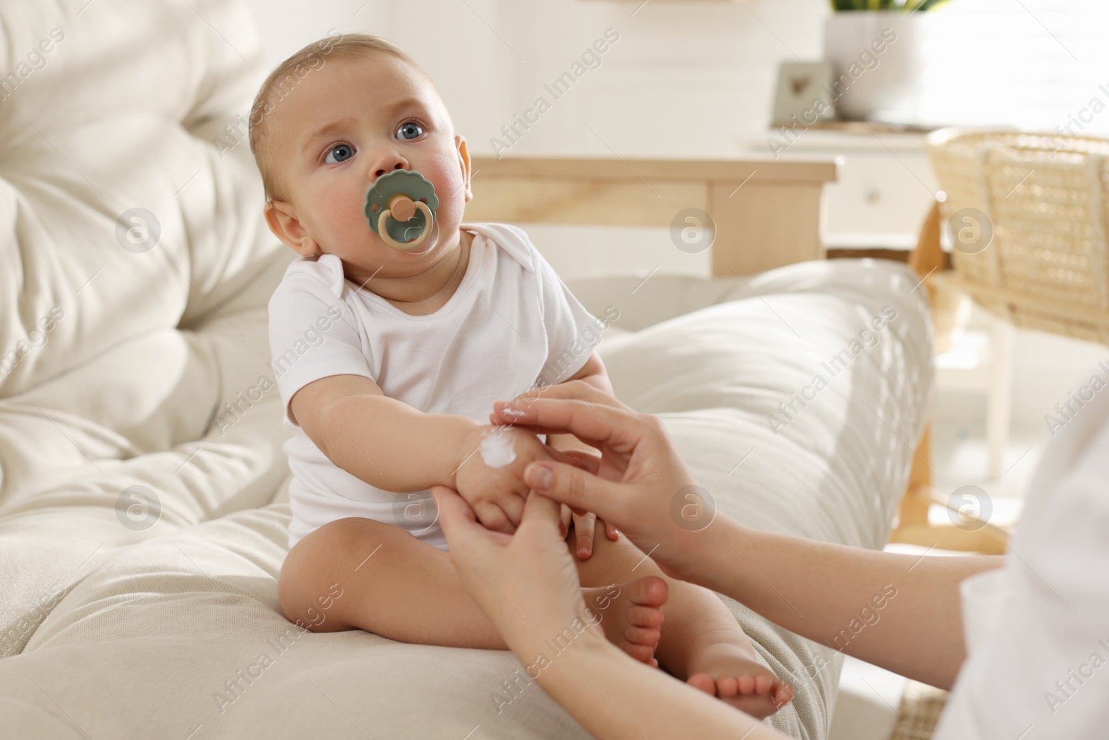 Photo of Mother applying body cream on her little baby at home, closeup