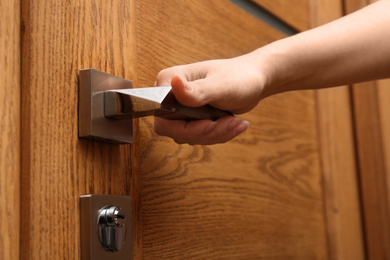 Woman opening wooden door indoors, closeup view