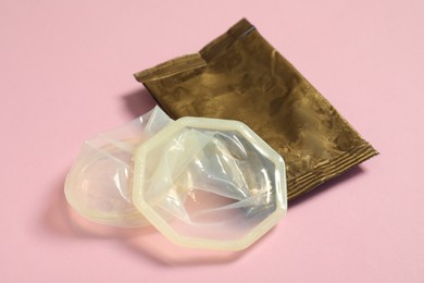Unrolled female condom and torn package on light pink background, closeup. Safe sex