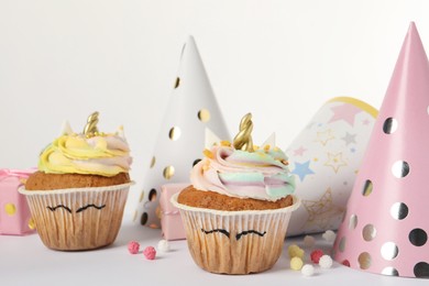 Photo of Cute sweet unicorn cupcakes and party hats on white table