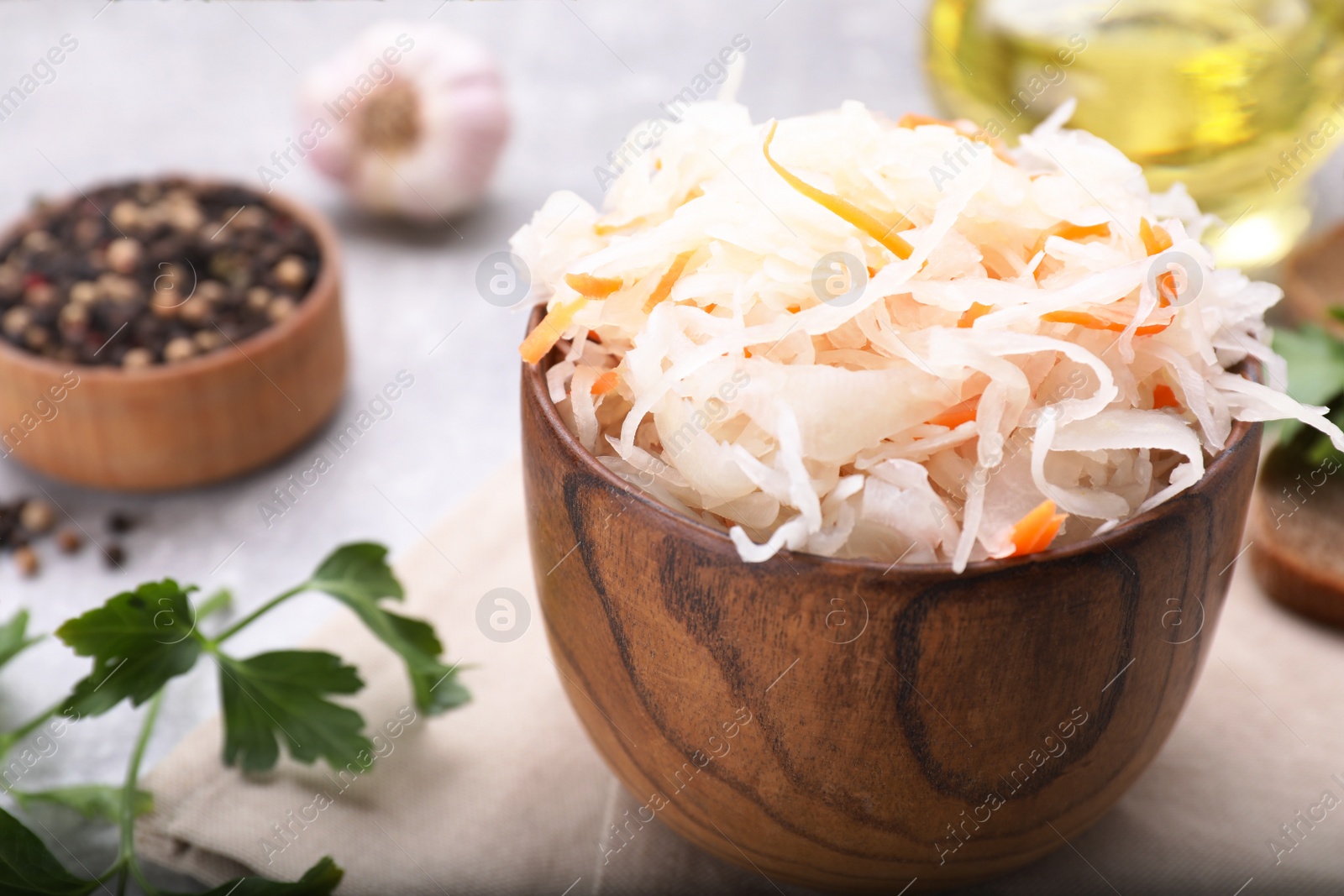 Photo of Bowl of tasty sauerkraut and ingredients on grey table, closeup