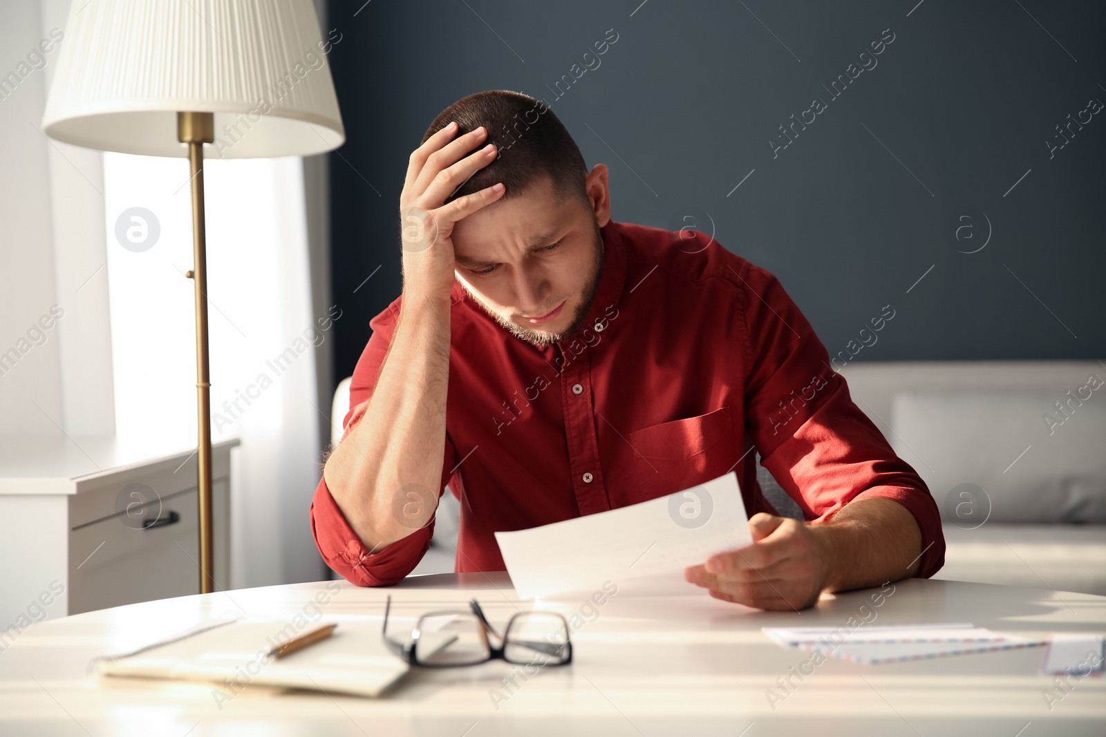 Photo of Man reading paper letter at white table in room