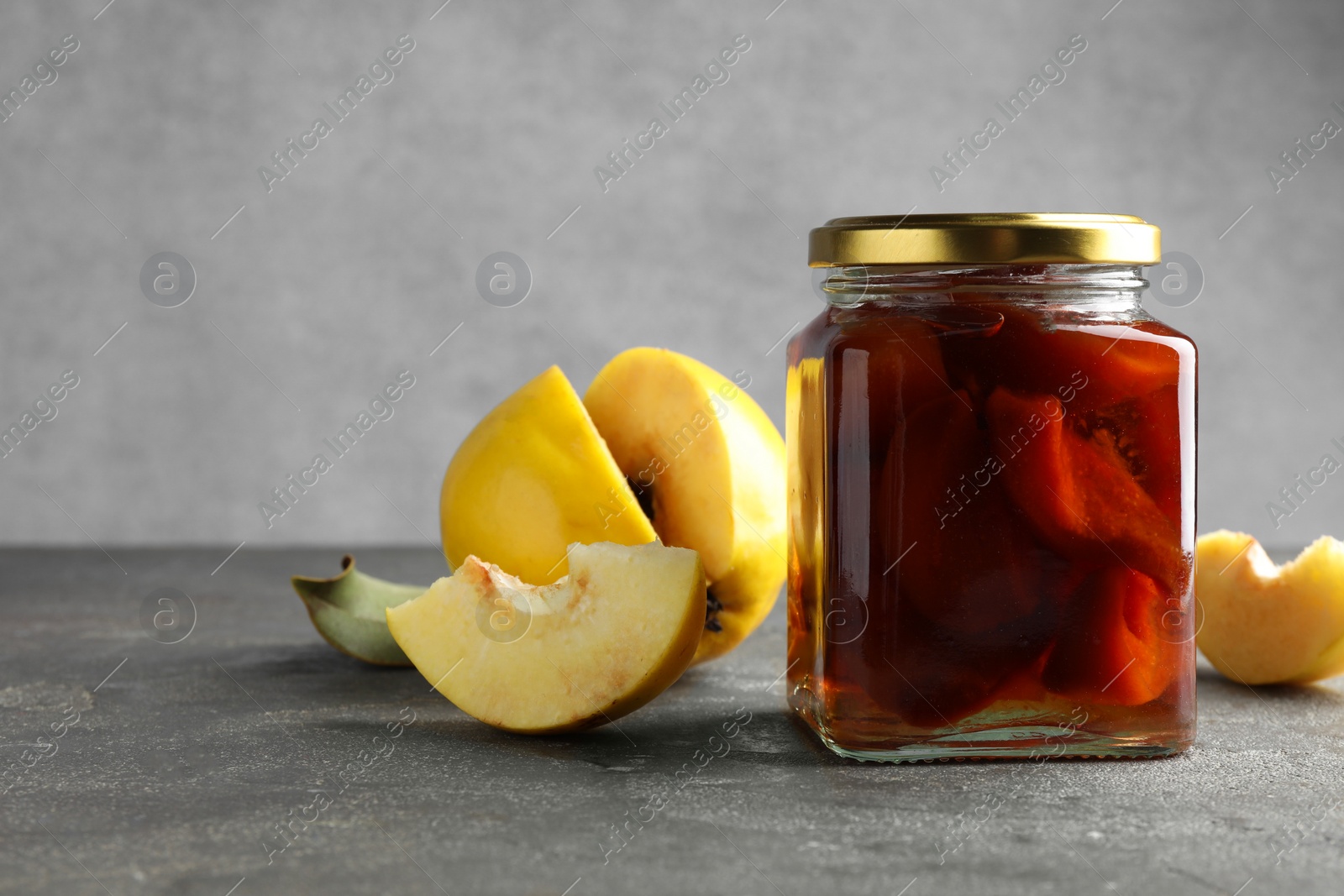 Photo of Tasty homemade quince jam in jar and fruits on grey textured table. Space for text