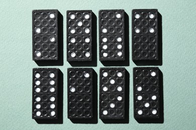 Photo of Set of black domino tiles on light green background, flat lay