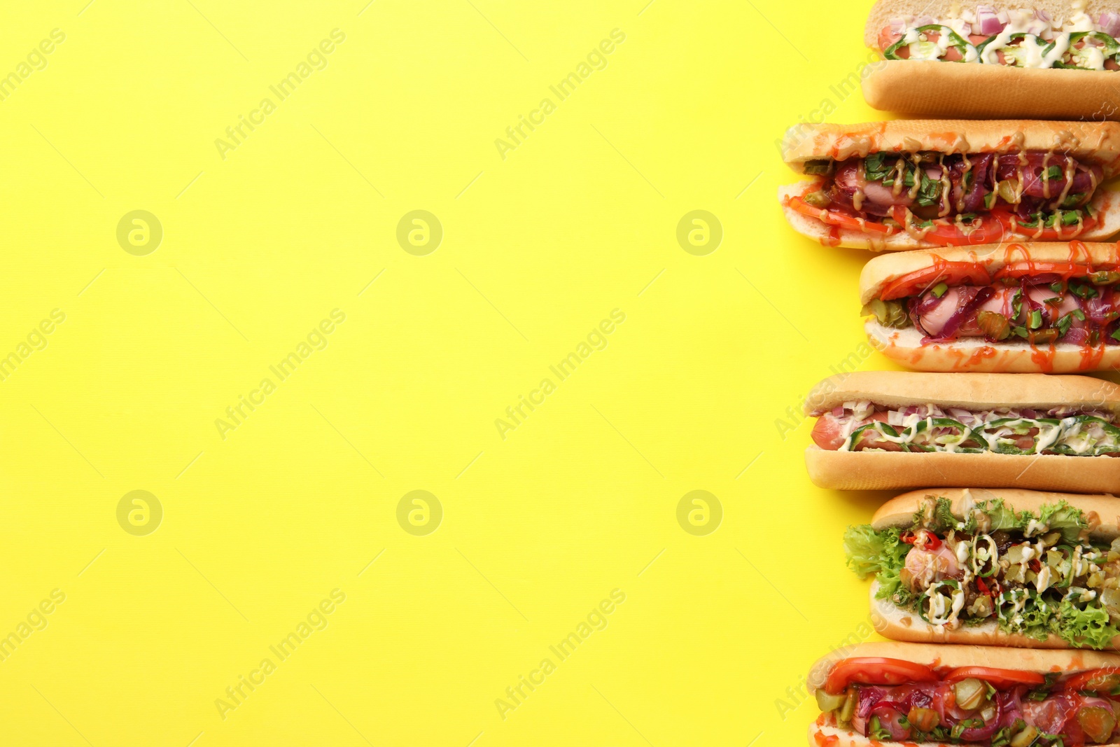 Photo of Delicious hot dogs with different toppings on yellow background, flat lay. Space for text