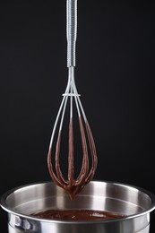 Photo of Chocolate cream flowing from whisk into bowl on black background