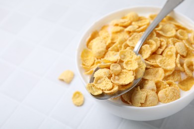 Photo of Breakfast cereal. Tasty corn flakes with milk in bowl and spoon on white tiled table, closeup. Space for text