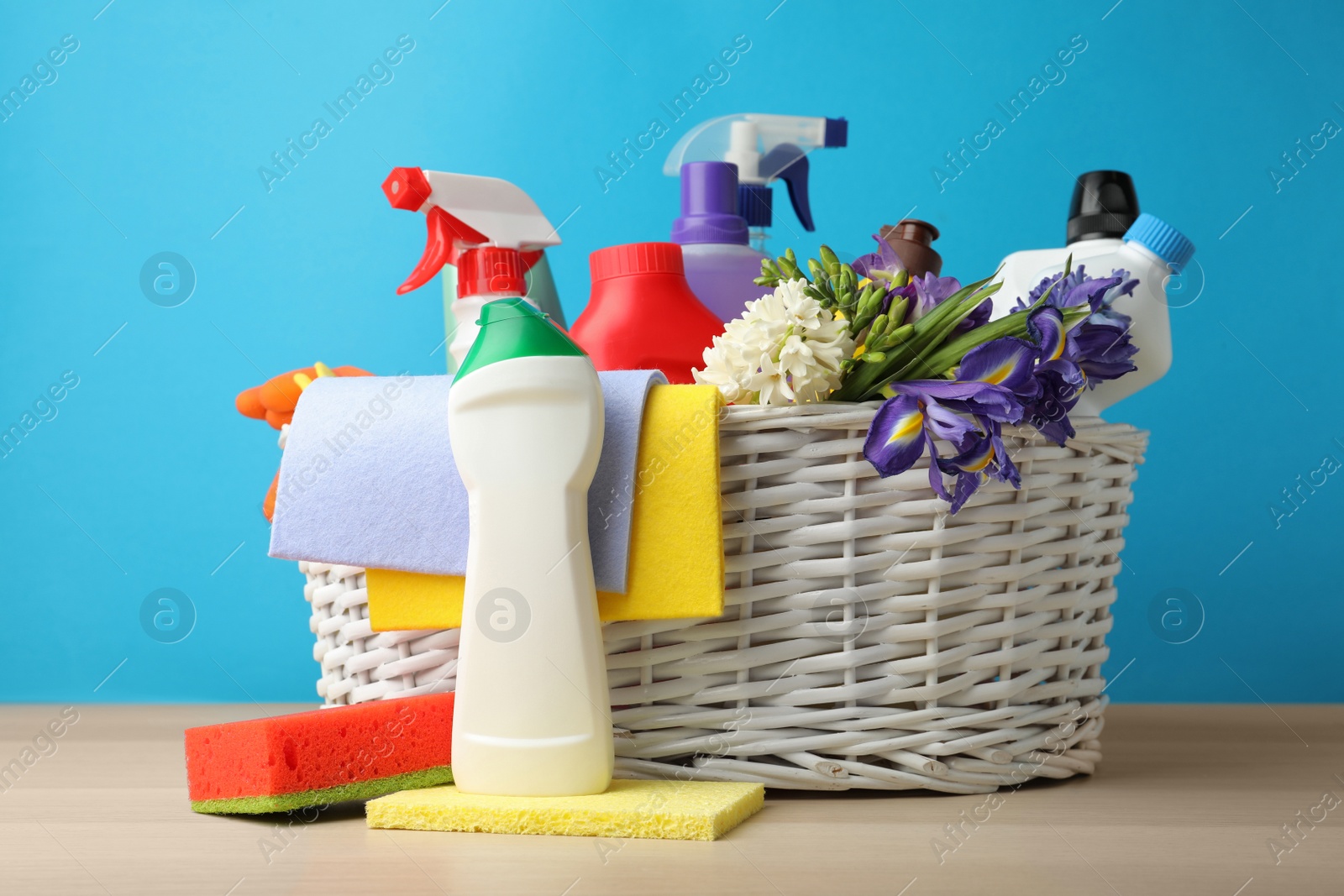 Photo of Wicker basket with spring flowers and cleaning supplies on wooden table