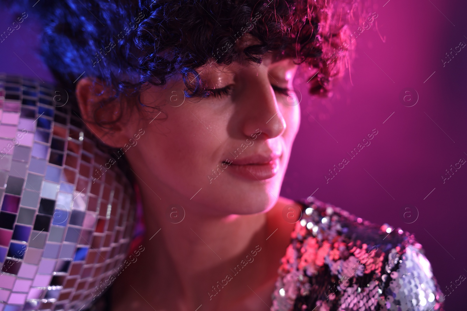 Photo of Beautiful young woman with disco ball posing on color background in neon lights, closeup