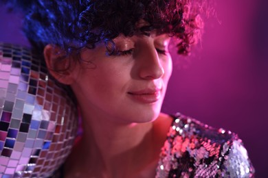 Photo of Beautiful young woman with disco ball posing on color background in neon lights, closeup