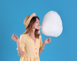 Photo of Happy young woman eating cotton candy on blue background. Space for text