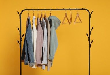 Rack with stylish clothes on wooden hangers against orange background