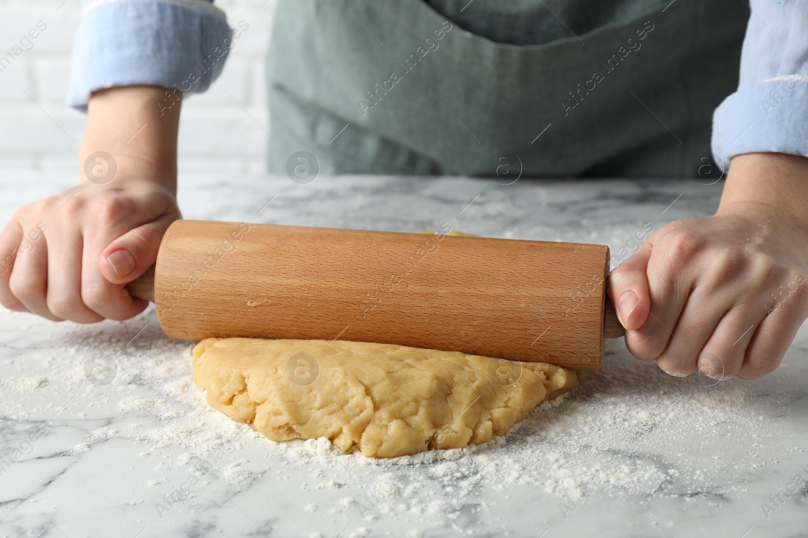 Photo of Making shortcrust pastry. Woman rolling raw dough at white marble table, closeup