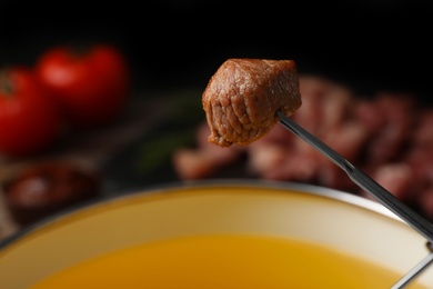 Photo of Fried piece of meat on fondue fork against blurred background. Space for text