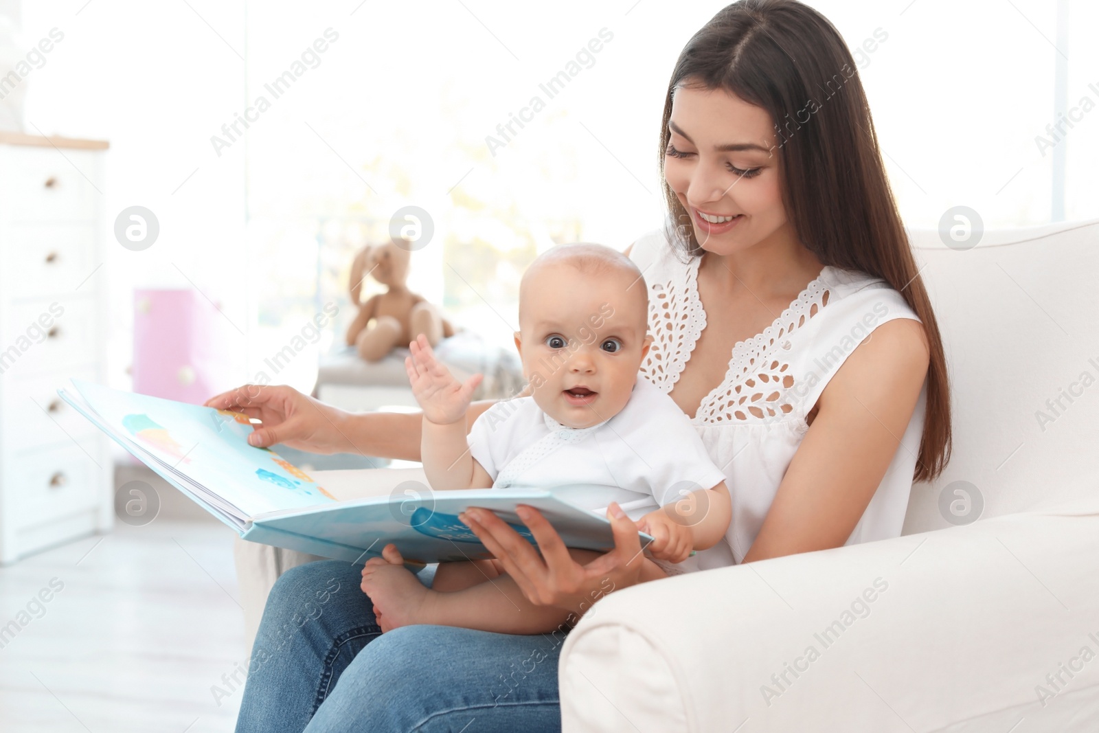 Photo of Young mother with her cute baby girl reading book in armchair at home