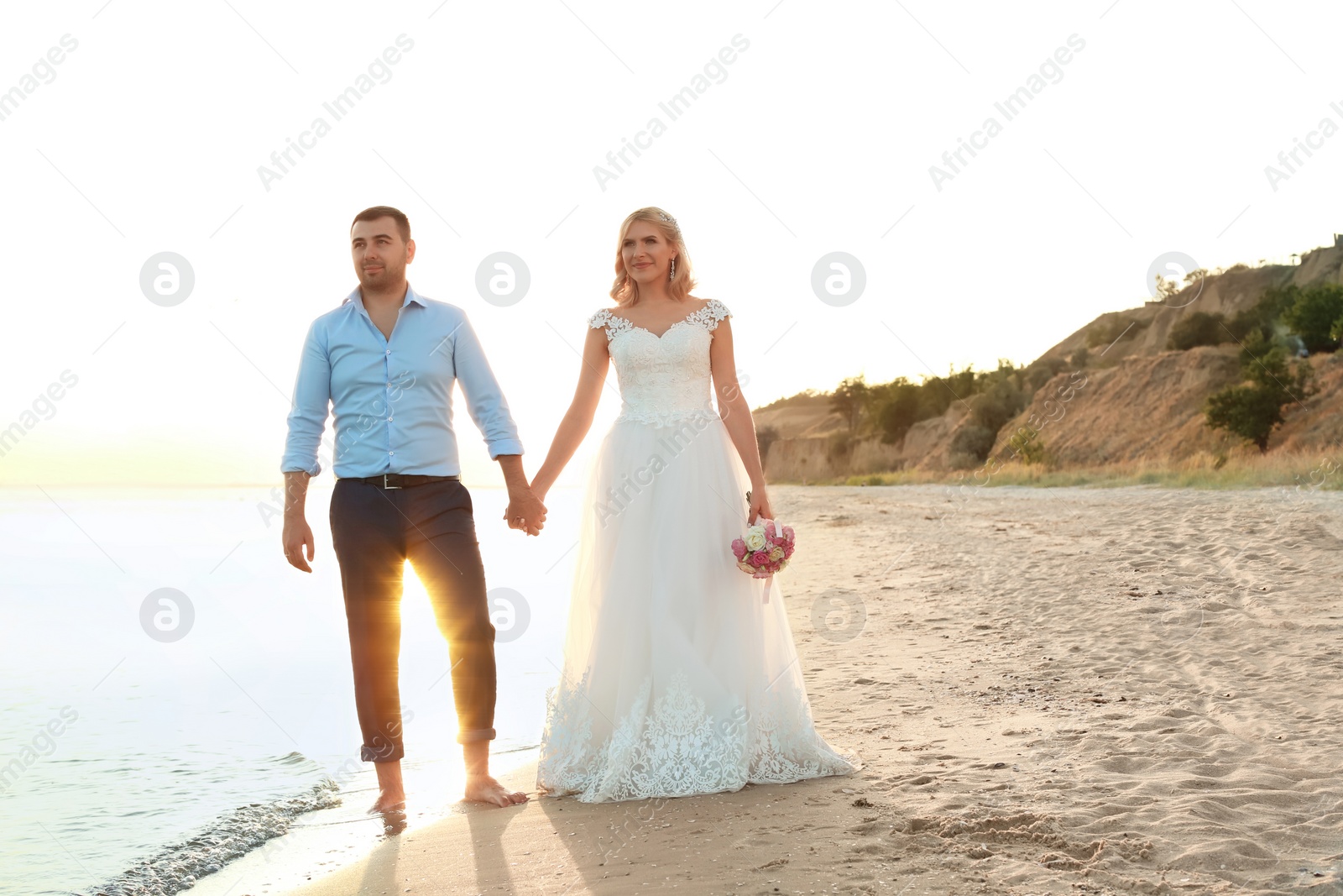 Photo of Wedding couple holding hands together on beach. Space for text