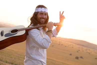 Photo of Happy hippie man with guitar showing peace sign in field, space for text