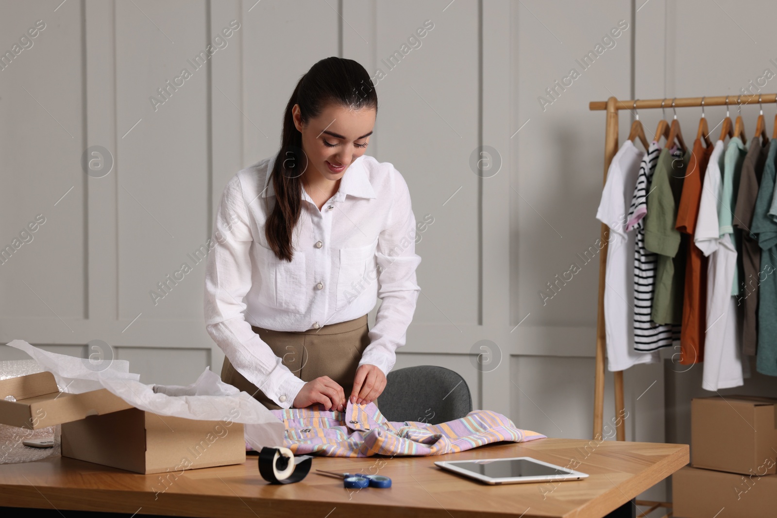 Photo of Seller packing shirt at table in office. Online store