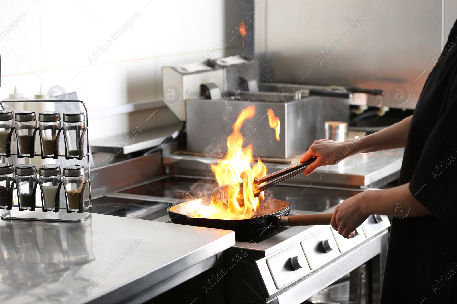 Photo of Female chef cooking meat with burning flame on stove in restaurant kitchen, closeup