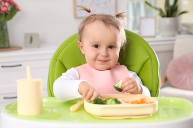 Photo of Cute little baby eating food in high chair at home